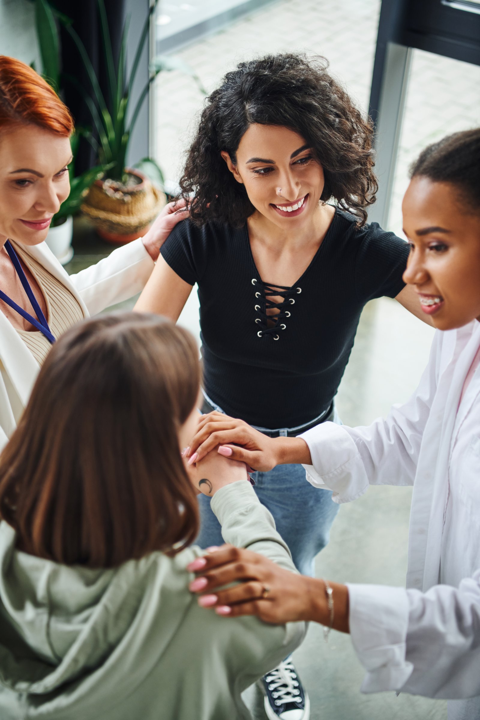 high angle view of diverse group of pleased multicultural women joining hands near positive